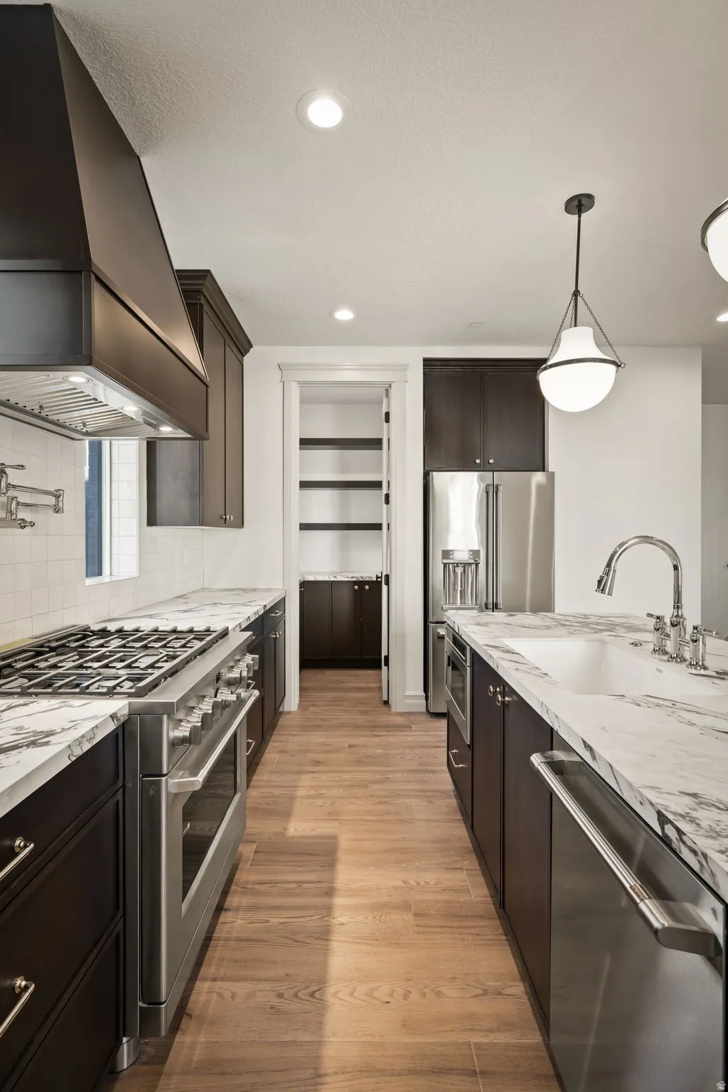 Kitchen featuring high end appliances, light stone countertops, light wood-style flooring, decorative backsplash, and dark wood finish cabinetry
