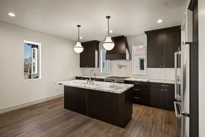 Kitchen featuring high end fridge, dark wood finish cabinets, a kitchen island with sink, light stone counters, and dark wood-type flooring