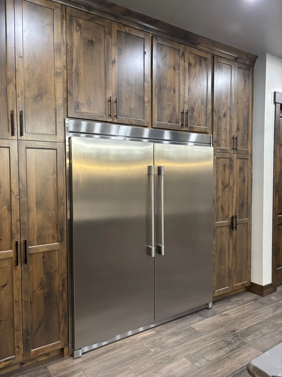 Kitchen with stainless steel built in fridge, dark wood-style flooring, and dark wood finish cabinetry