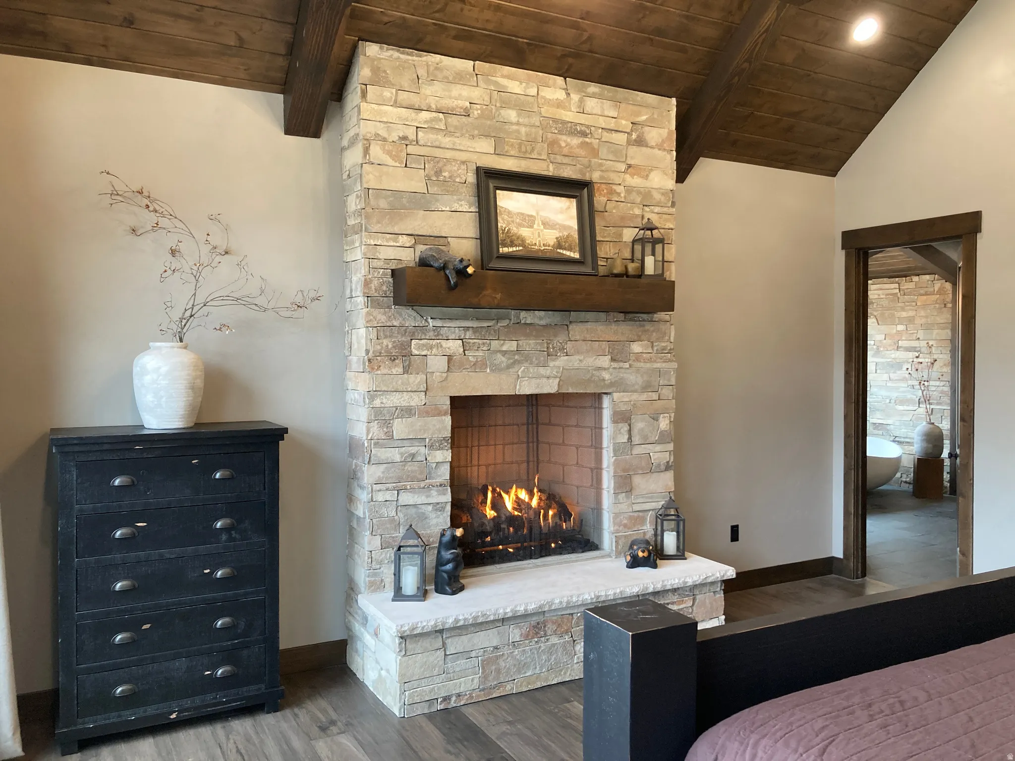 Bedroom featuring a stone fireplace, wooden ceiling, lofted ceiling with beams, and wood finished floors