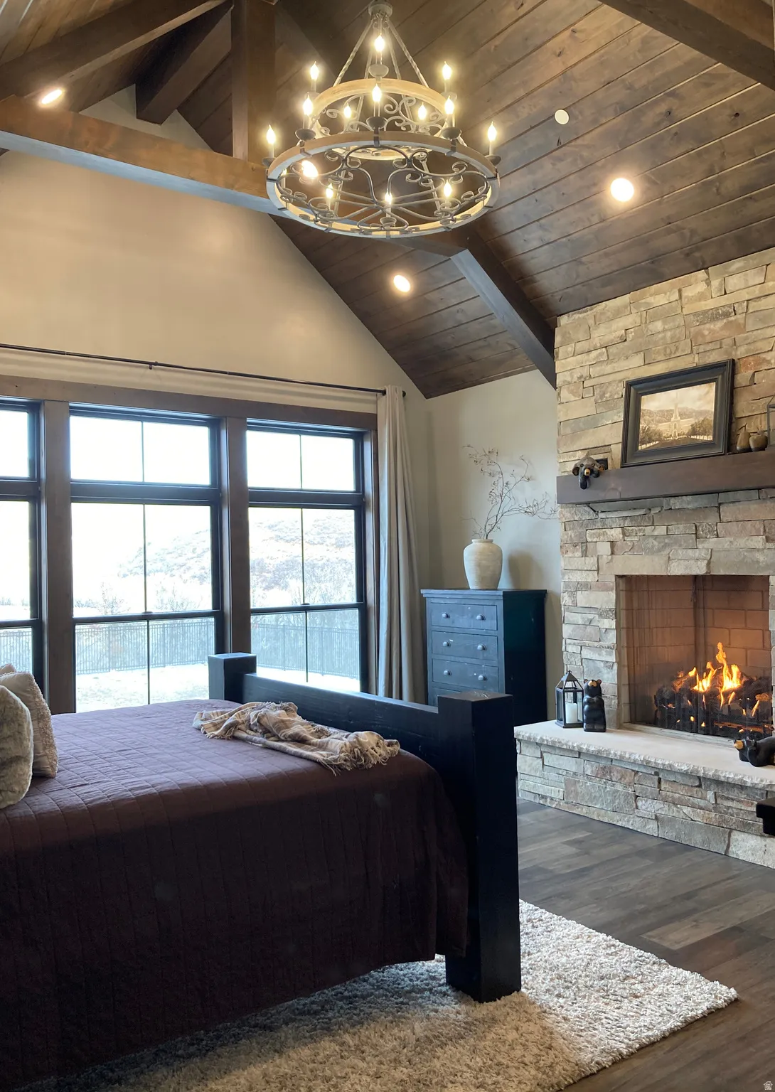 Bedroom with a high wood beamed ceiling, dark wood-style flooring, a fireplace, and a chandelier
