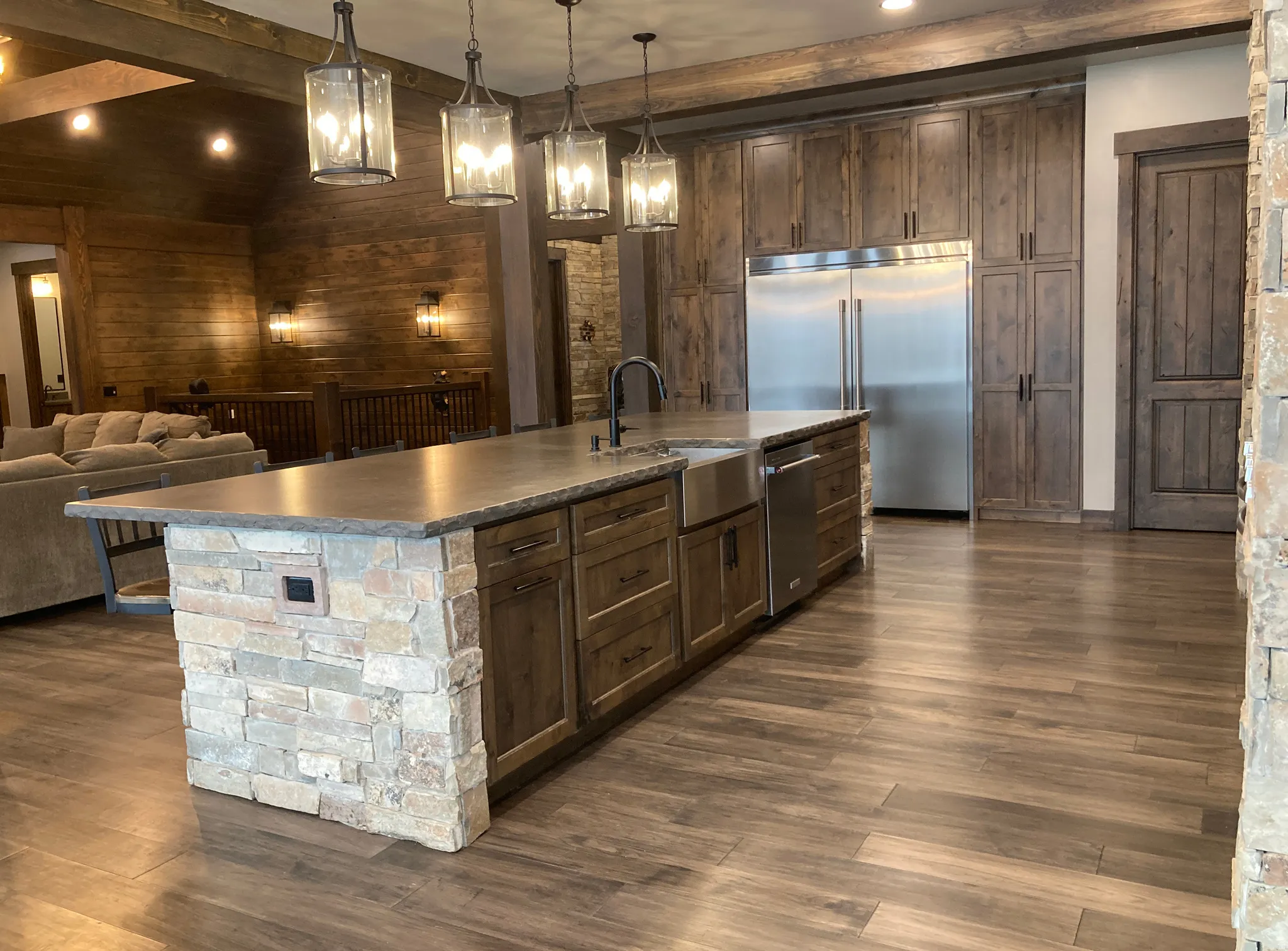 Kitchen featuring a large island with sink, stainless steel appliances, open floor plan, dark wood finished floors, and hanging light fixtures