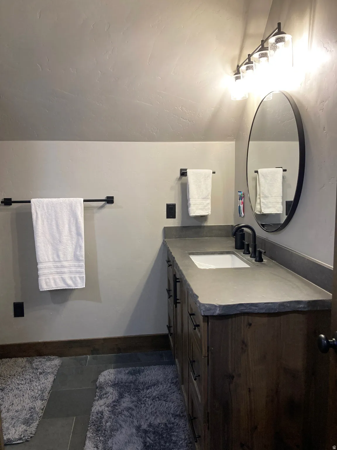 Half bathroom with vanity, dark tile patterned flooring, and lofted ceiling