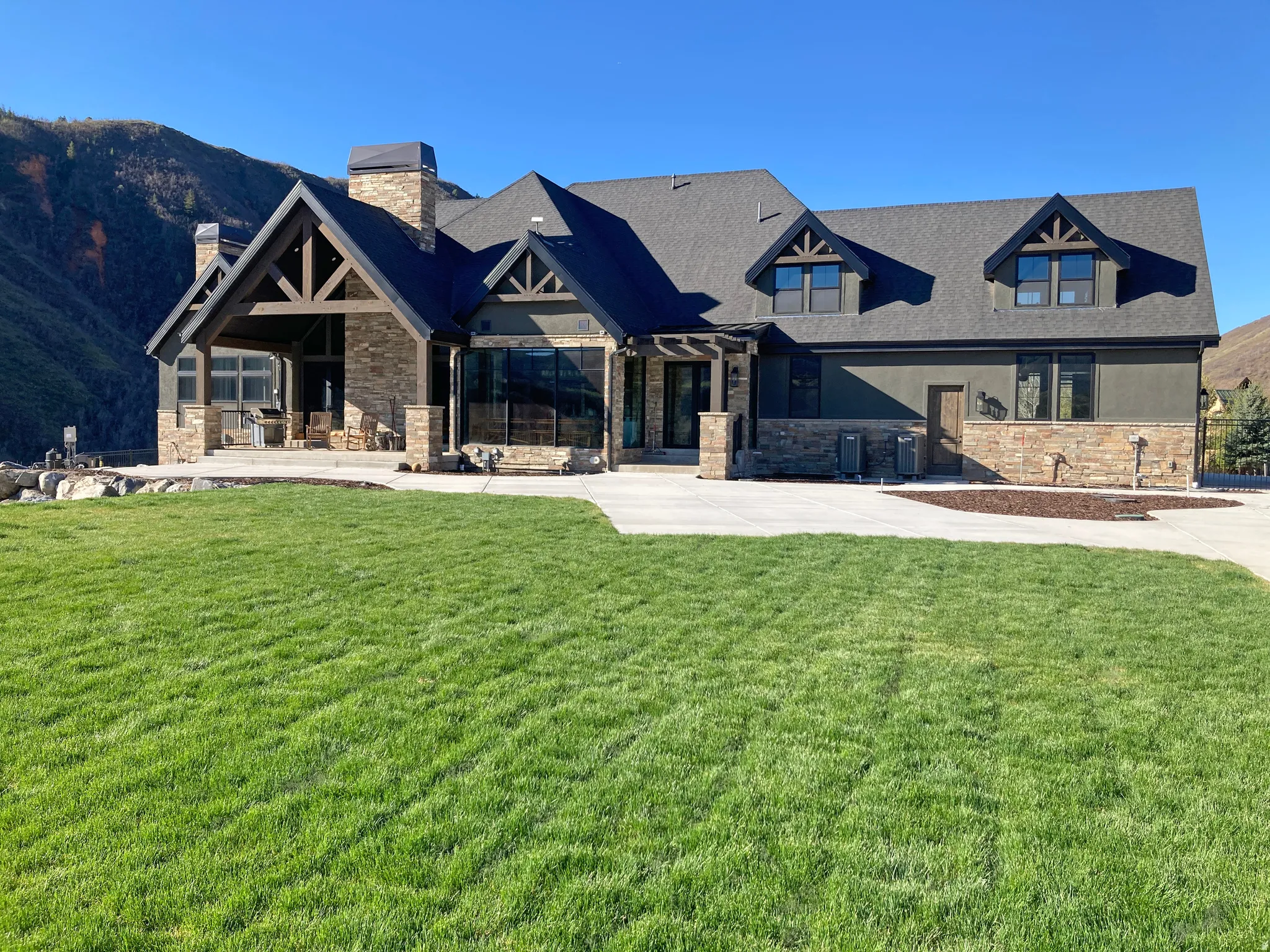 View of rear of property featuring stone siding, a front lawn, a chimney, a mountain view, and stucco siding