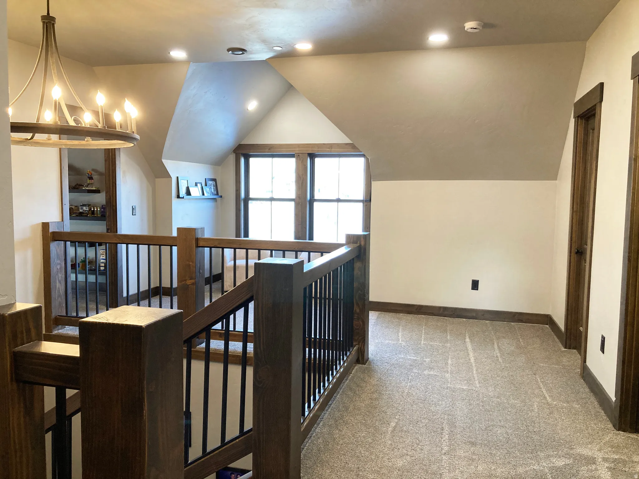 Hallway with light colored carpet, vaulted ceiling, an upstairs landing, and suspended lighting
