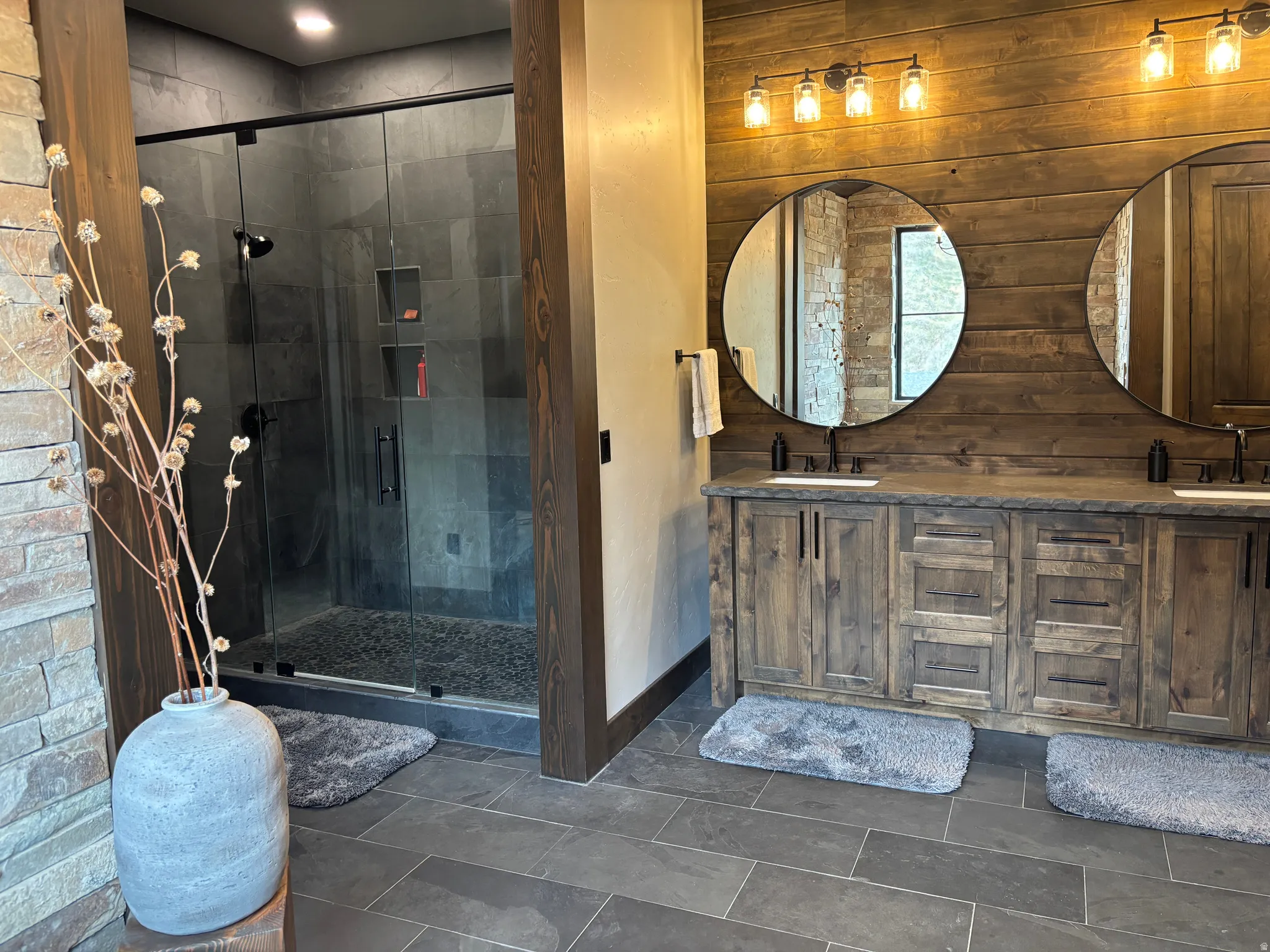 Bathroom with double vanity, wooden walls, and a shower stall