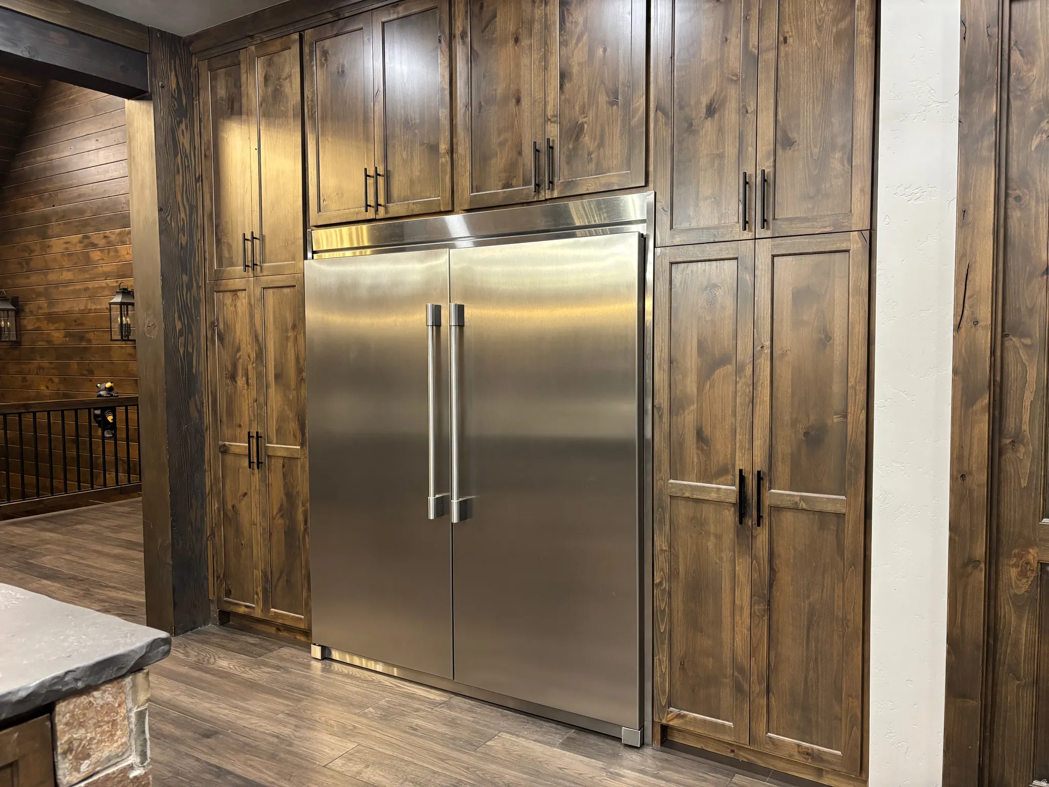 Kitchen with built in refrigerator, wooden walls, dark wood-type flooring, dark wood finish cabinetry, and beamed ceiling