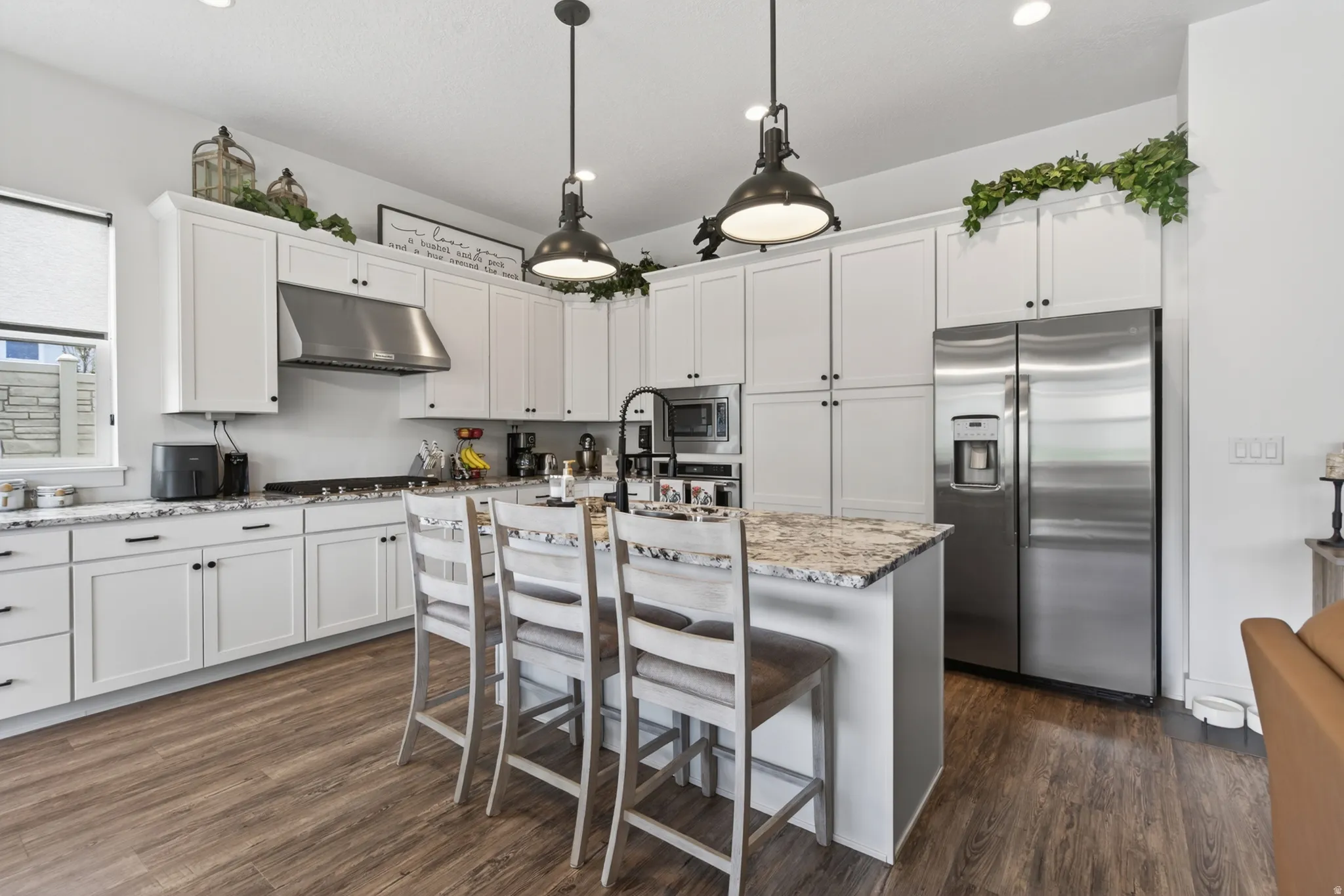 Kitchen with stainless steel appliances, light stone counters, white cabinetry, and an island with sink