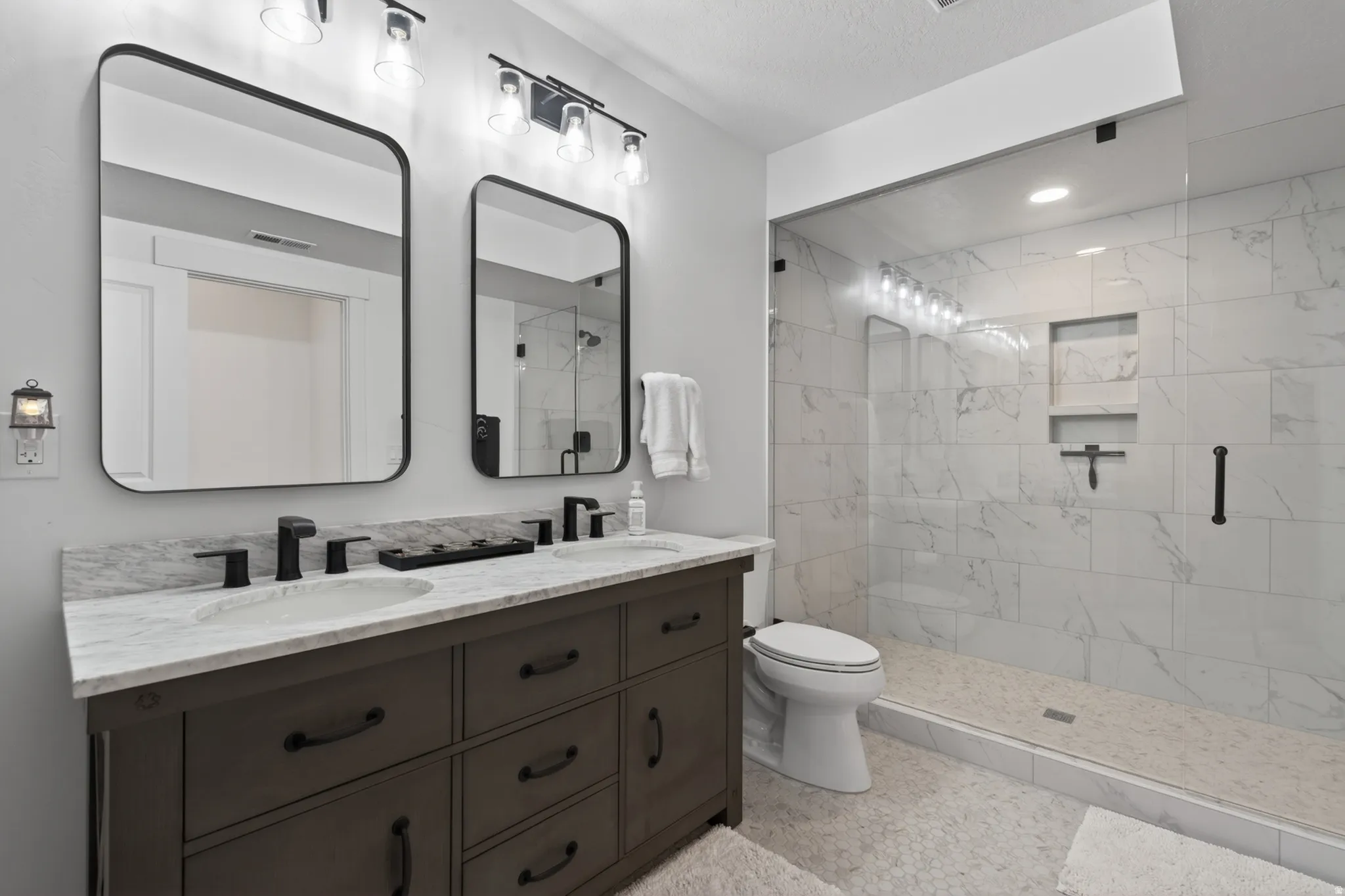 Full bath featuring double vanity and a marble finish shower
