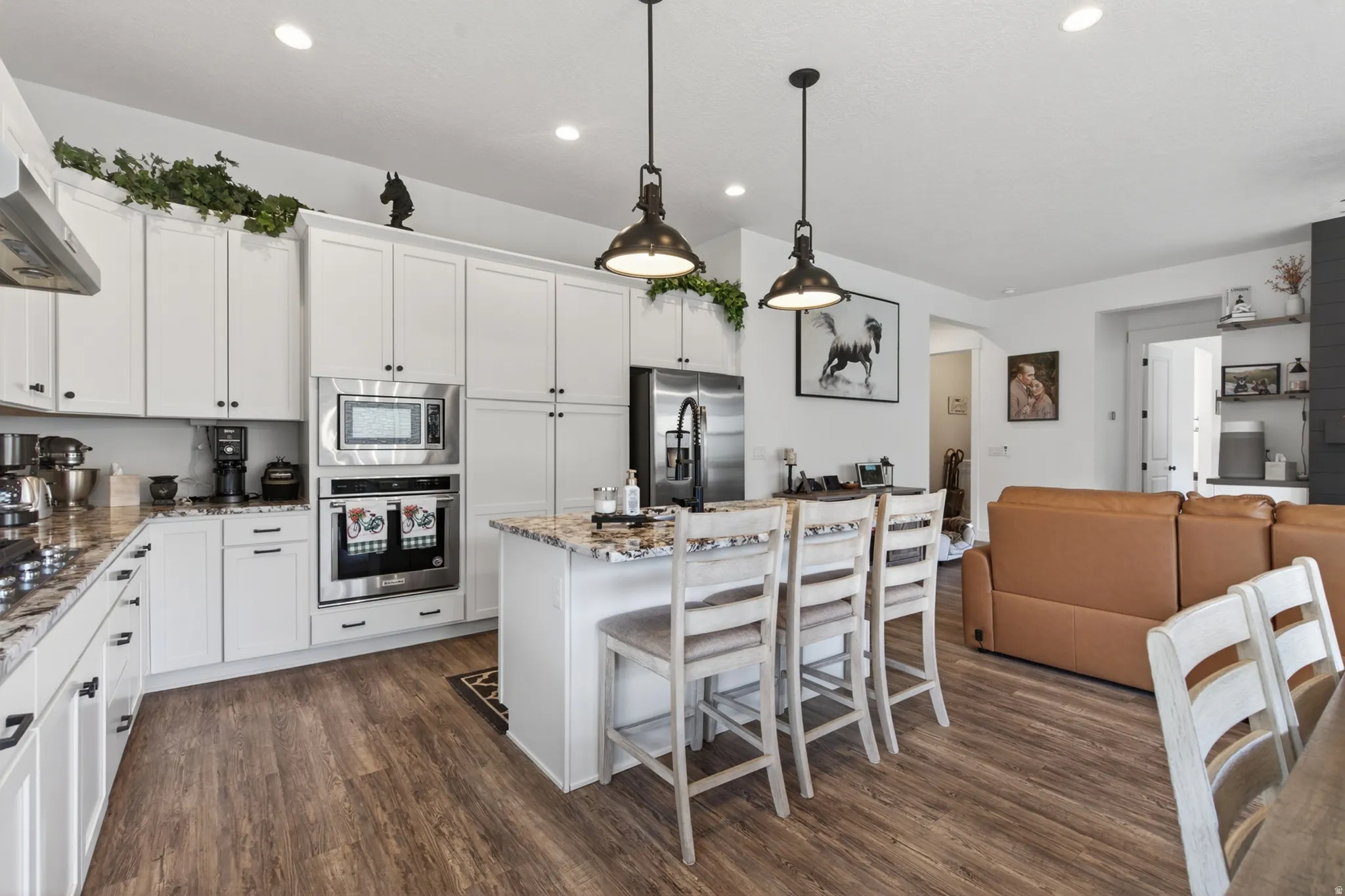 Kitchen with open floor plan, white cabinetry, stainless steel appliances, and light stone counters