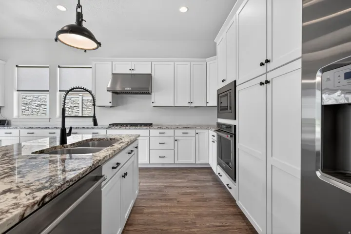 Gourmet kitchen featuring white shaker cabinetry, stainless steel appliances, granite countertops, wood-finish flooring, and a large center island with an undermount sink