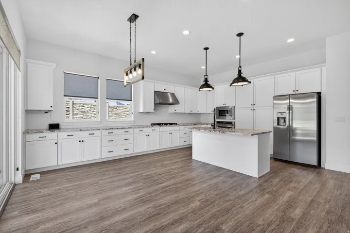 Spacious kitchen featuring white cabinetry, stainless steel appliances, a center island with pendant lighting, and wood-finish flooring