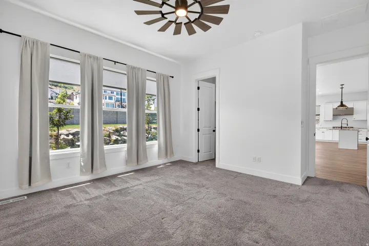 Carpeted room with a multi-paneled ceiling fan and four tall windows