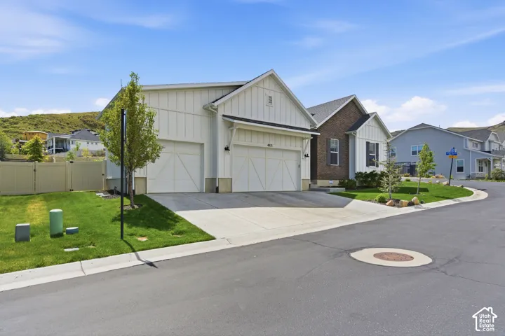 Single-story exterior featuring white vertical siding, brick veneer accents, a three-car garage with carriage-style doors, and concrete driveway