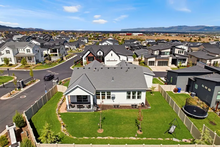 Pitched roof architecture with a covered patio, extensive fenced backyard, and a surrounding neighborhood
