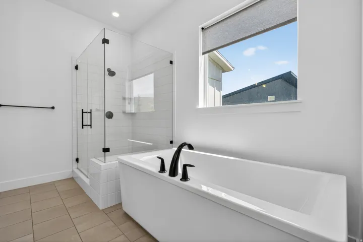 Bathroom featuring a freestanding soaking tub with matte black fixtures, a glass-enclosed shower with subway tile surround, and light-toned tile flooring