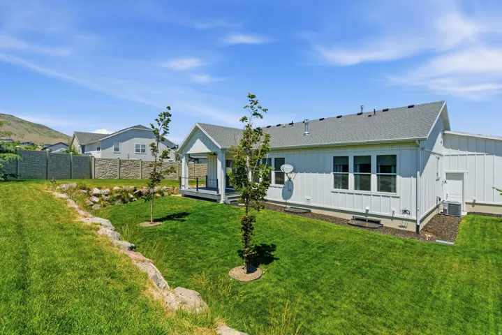 Expansive backyard featuring a manicured lawn, established landscaping, and a covered patio