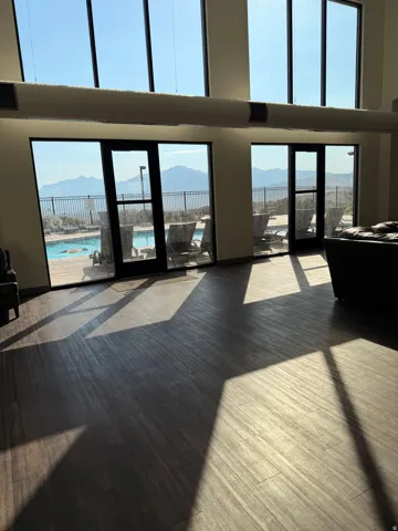 Spacious interior with wood-finish flooring, featuring expansive floor-to-ceiling windows and glass doors opening to an outdoor pool area