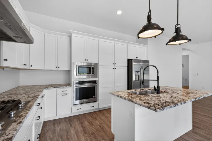 Open-concept kitchen featuring white cabinetry, stainless steel appliances, and a central island with a dual-basin sink and a black gooseneck faucet