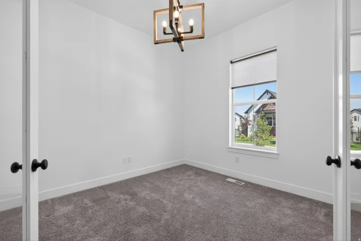 Neutral tone interior featuring a modern ceiling fixture, a window with a roller shade, white trim, and gray carpet flooring