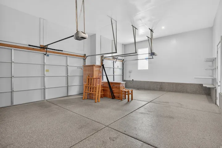 Spacious garage featuring a durable epoxy floor, built-in shelving, two overhead garage doors, and a window providing natural light