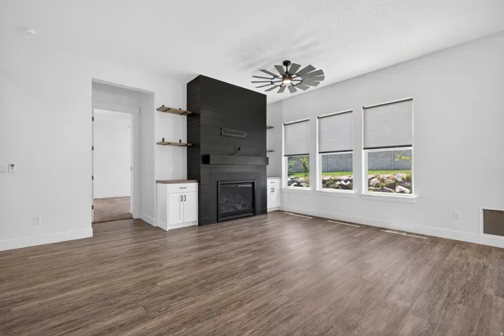 Spacious living area featuring wood-finish flooring, a contemporary fireplace with shiplap-style surround, built-in cabinetry, and multiple windows