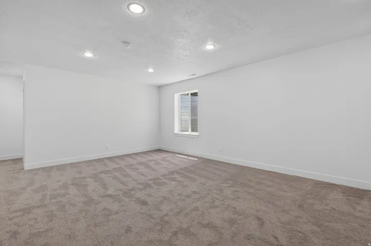 Spacious room featuring neutral carpeting, recessed ceiling lighting, and a single window with horizontal blinds