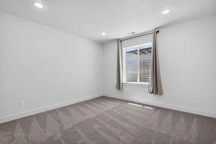 Room featuring light gray patterned carpeting, white walls, recessed ceiling lighting, a window with a window well, and white baseboards