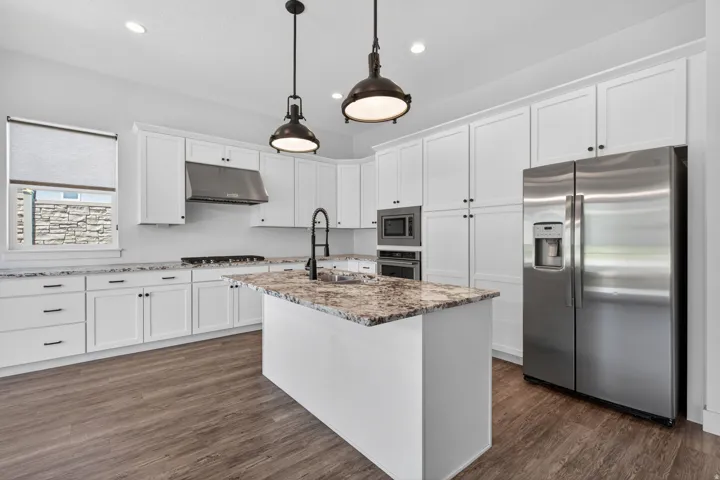 Modern kitchen featuring white shaker cabinetry, stainless steel appliances, a center island with a stone countertop, wood-finish flooring, and industrial-style pendant lighting