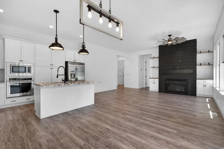 Open-concept living space featuring wood-finish flooring, a kitchen island with stone countertops, stainless steel appliances, and a gas fireplace with a shiplap surround