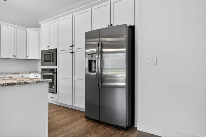 Kitchen featuring white shaker cabinetry, stainless steel side-by-side refrigerator, built-in microwave, and wood-finish flooring