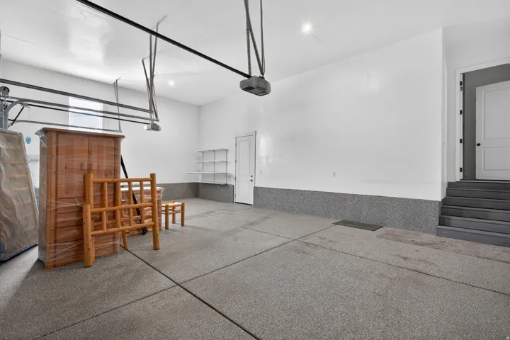 Spacious garage featuring a durable speckled epoxy floor, white painted walls, built-in shelving, and direct entry access