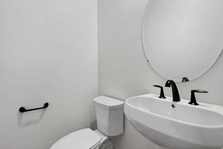 Pedestal sink with matte black faucet, oval mirror, and white toilet