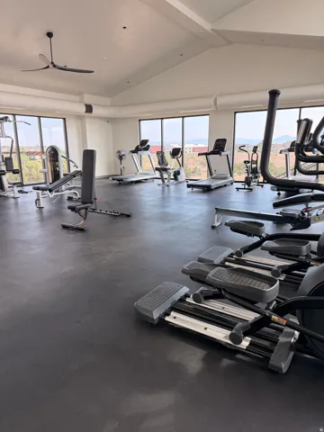 Spacious fitness center featuring expansive window walls, a vaulted ceiling with a modern ceiling fan, and durable rubber flooring