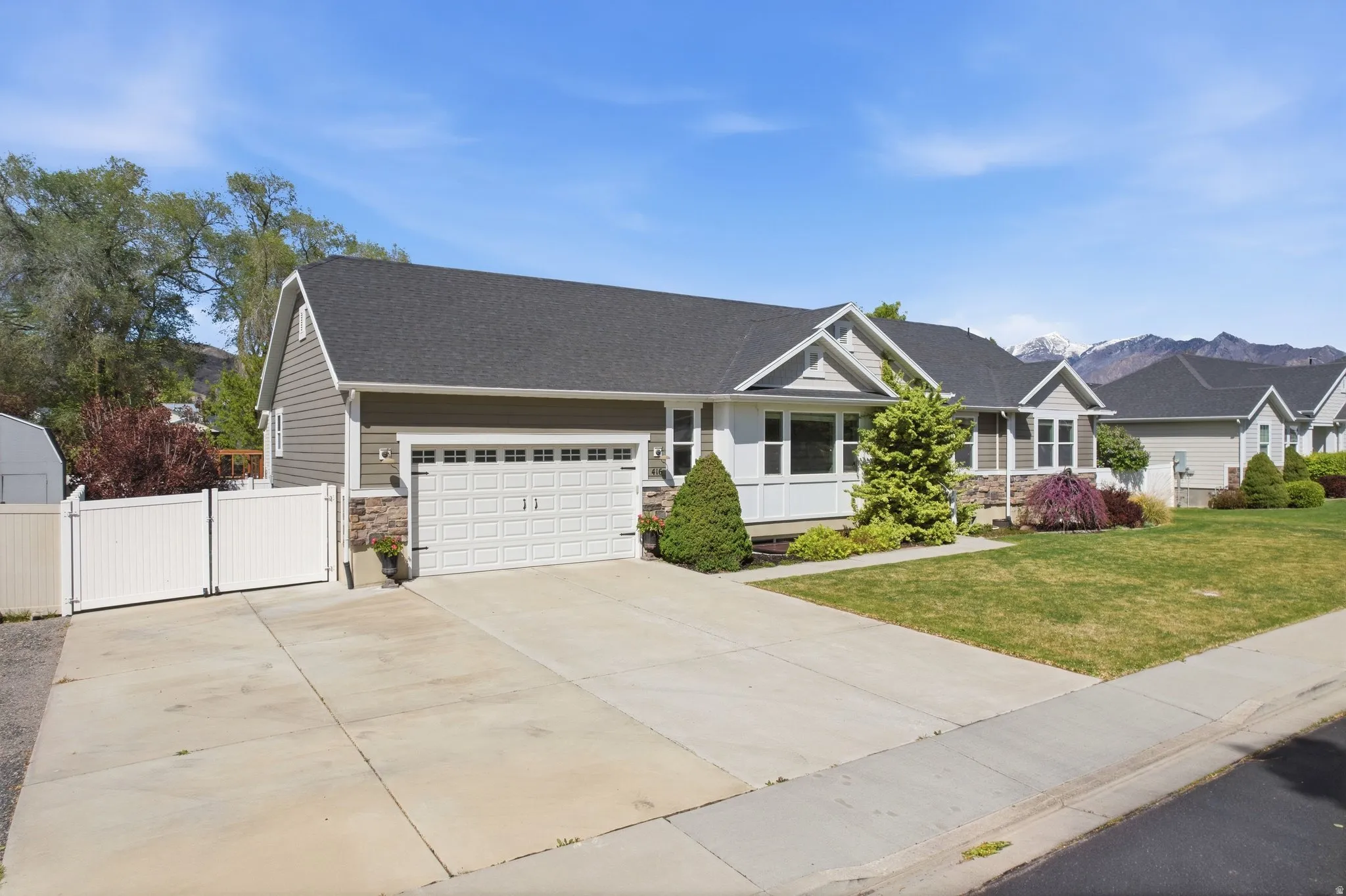 View of front of home featuring stone siding, concrete driveway, a gate, and a garage