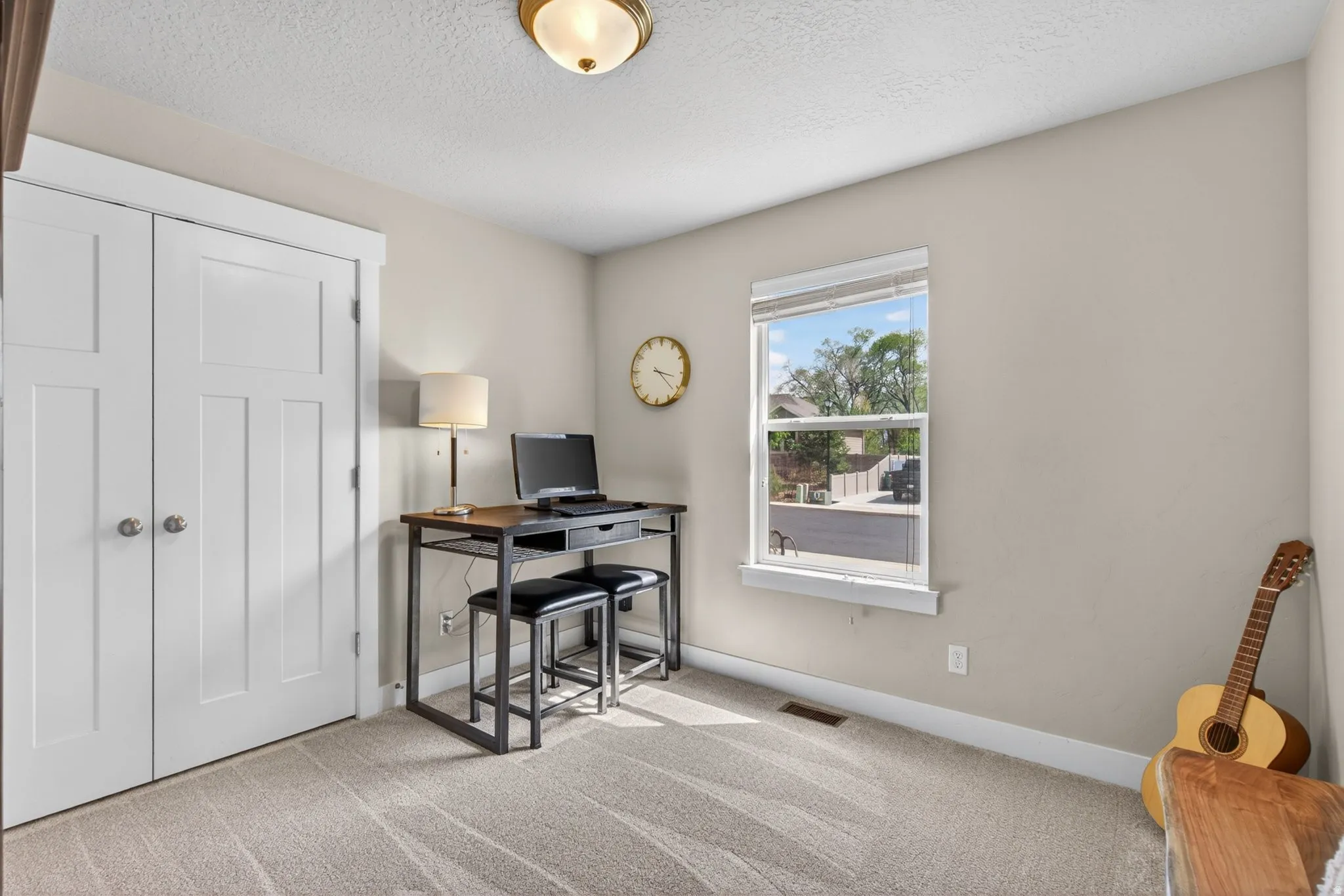 Home office with light colored carpet and a textured ceiling