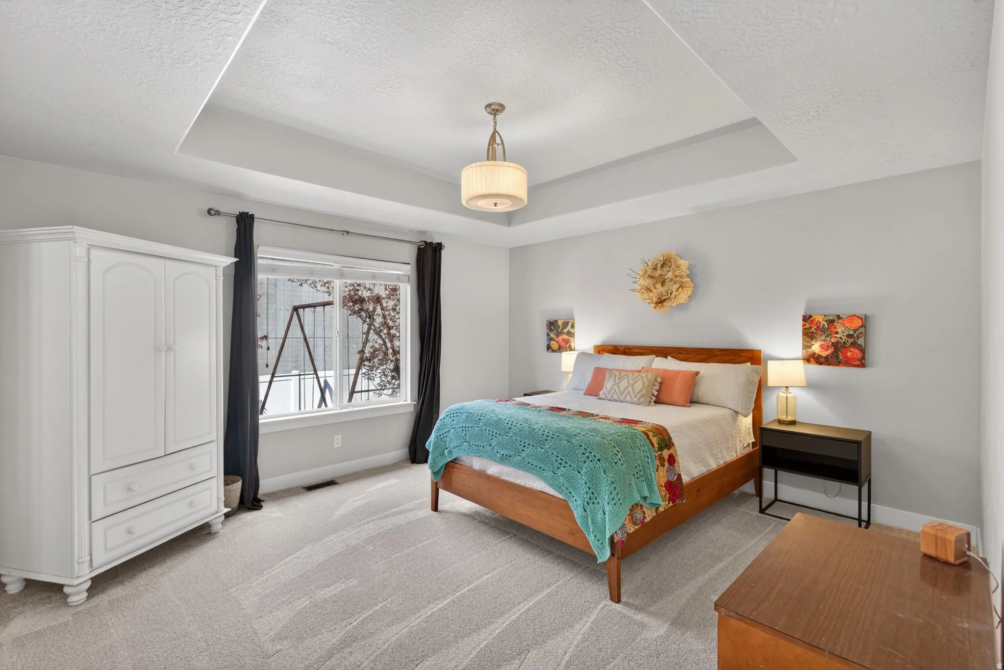 Bedroom with light colored carpet, a tray ceiling, and a textured ceiling