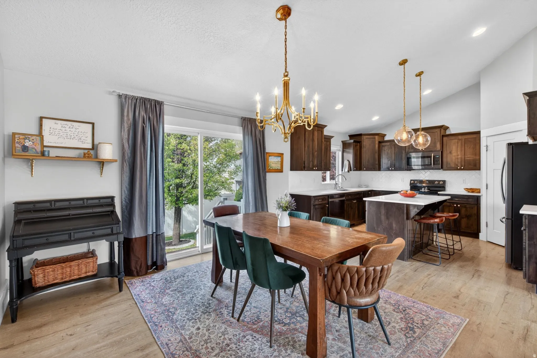 Dining area with suspended lighting, light wood-style floors, and vaulted ceiling