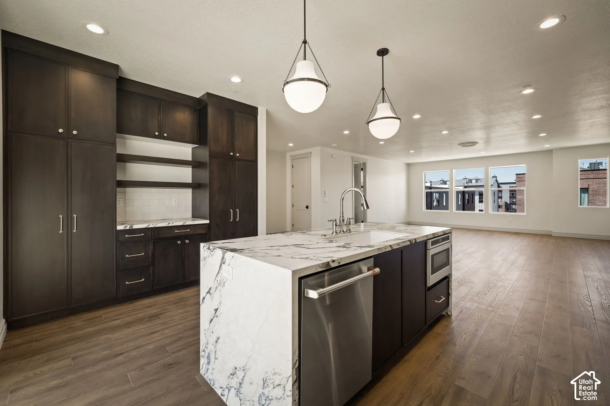 Kitchen with stainless steel appliances, light stone countertops, a kitchen island with sink, dark wood finished floors, and tasteful backsplash