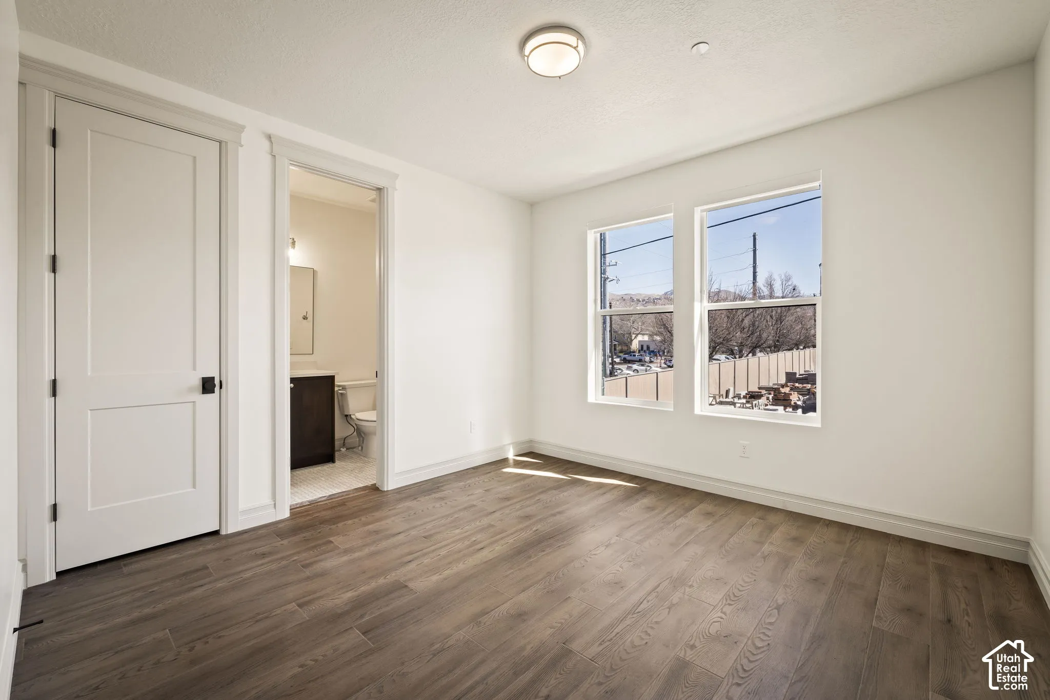 Unfurnished bedroom featuring ensuite bath and dark wood-type flooring