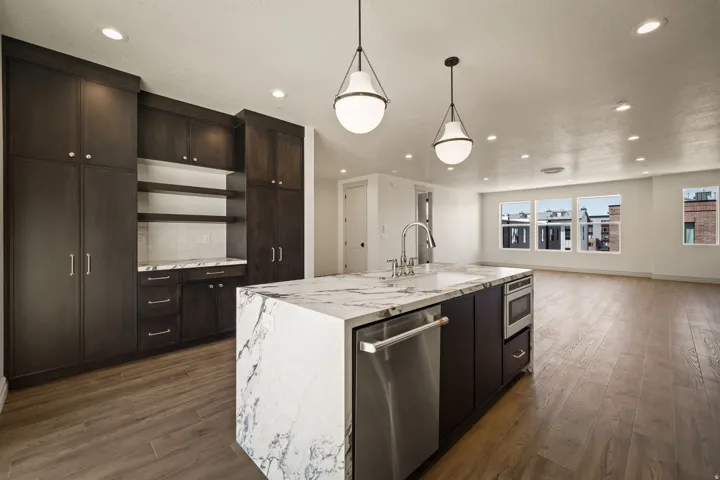 Kitchen with stainless steel appliances, light stone countertops, a kitchen island with sink, dark wood finished floors, and tasteful backsplash