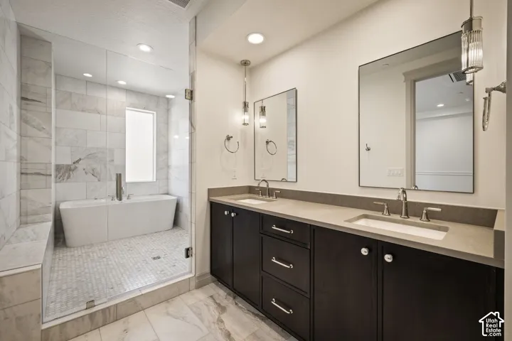 Full bath featuring double vanity, recessed lighting, a freestanding bath, light marble finish floors, and a stall shower