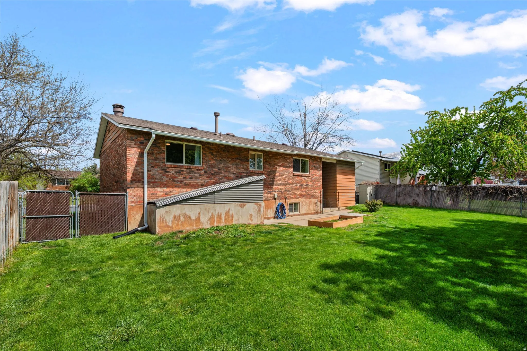 Rear view of property with a fenced backyard, a gate, a chimney, brick siding, and a deck