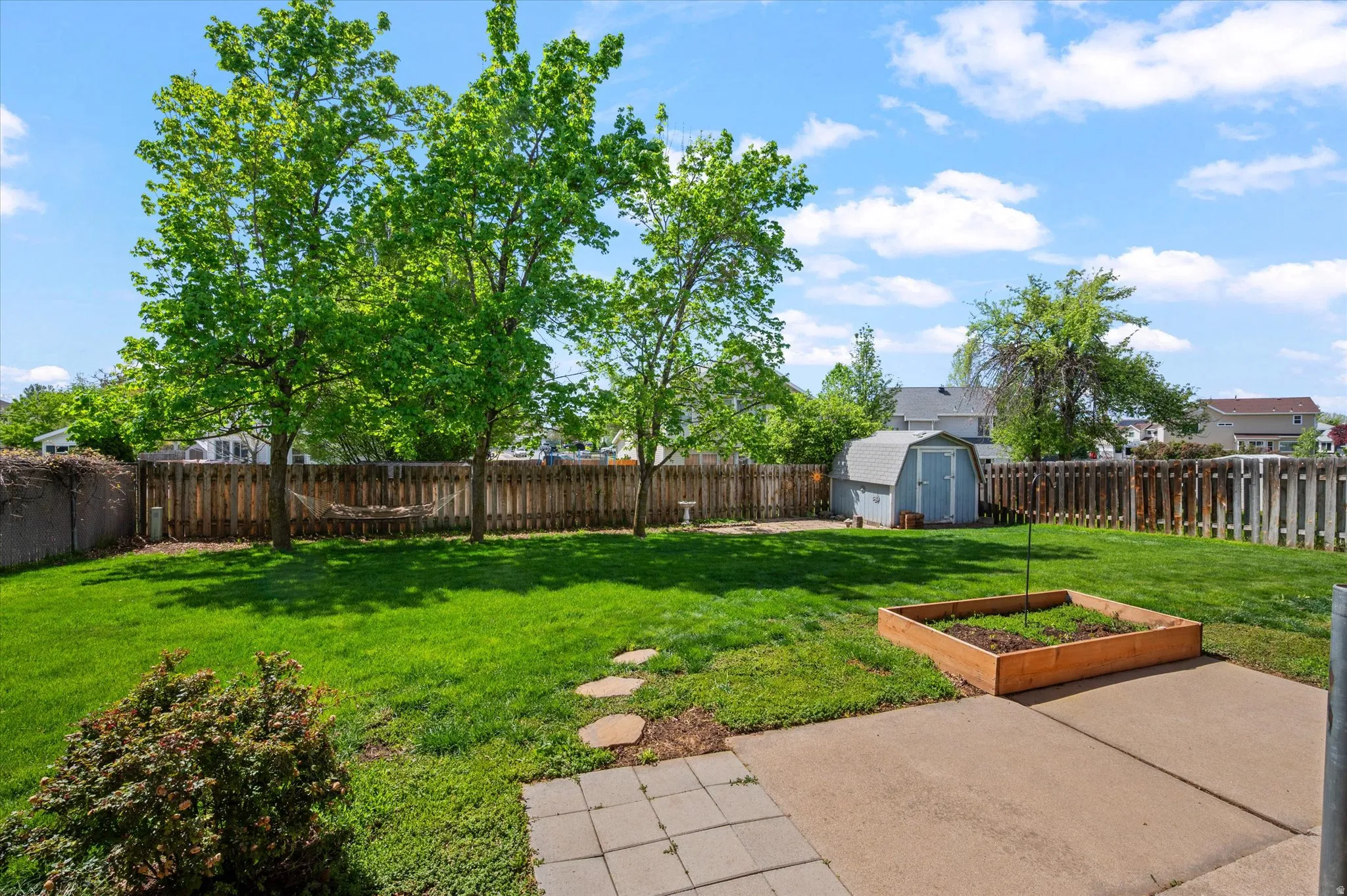 Fenced backyard featuring a storage shed, a patio area, and a vegetable garden