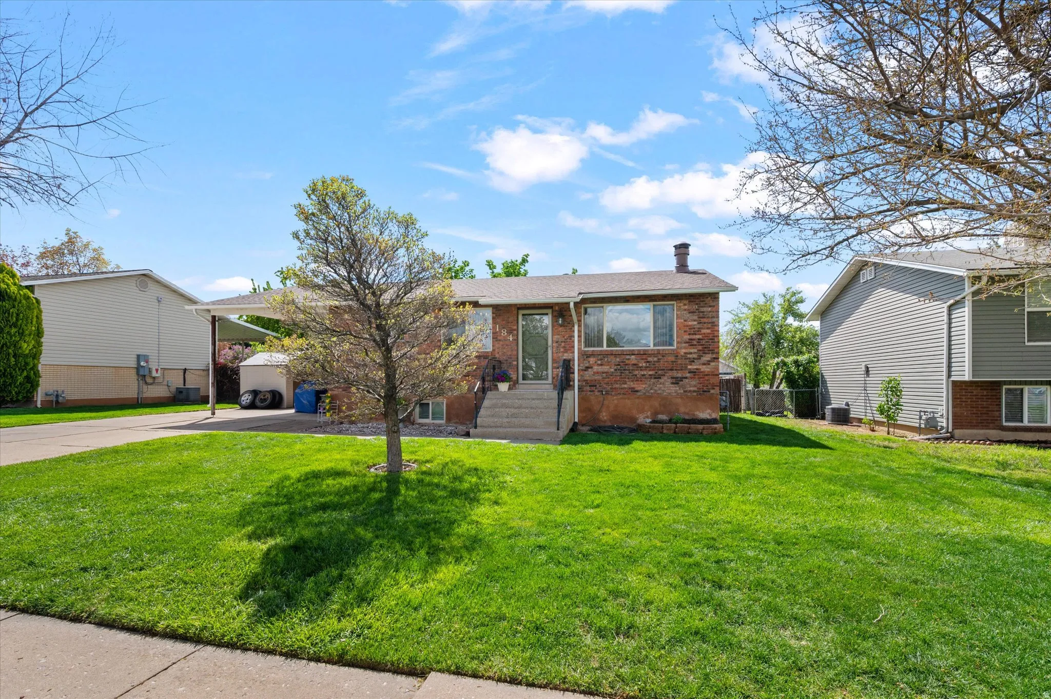 View of front facade with brick siding, driveway, a carport, a front yard, and a chimney