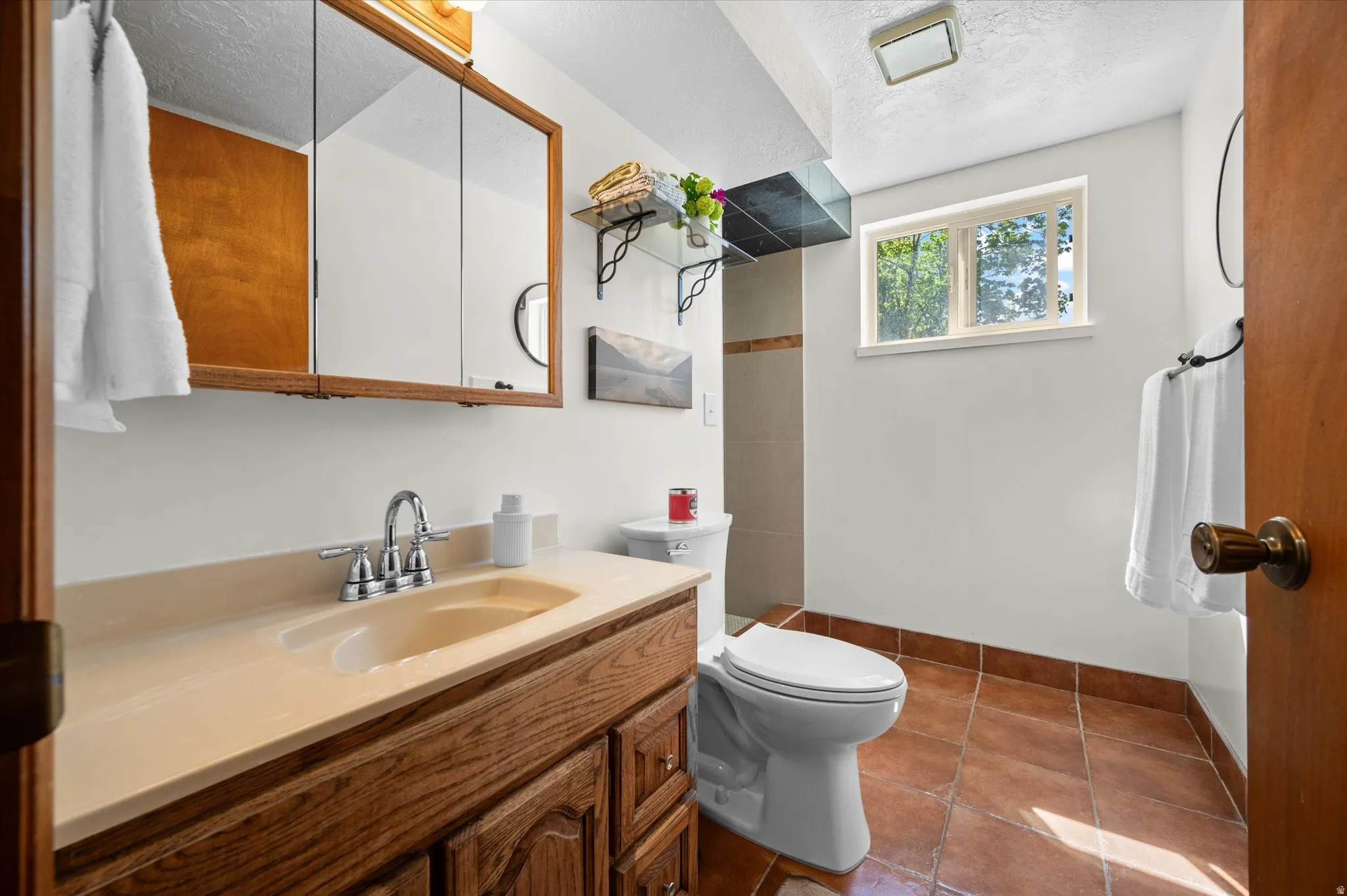 Bathroom featuring vanity, a textured ceiling, dark tile patterned floors, and a shower