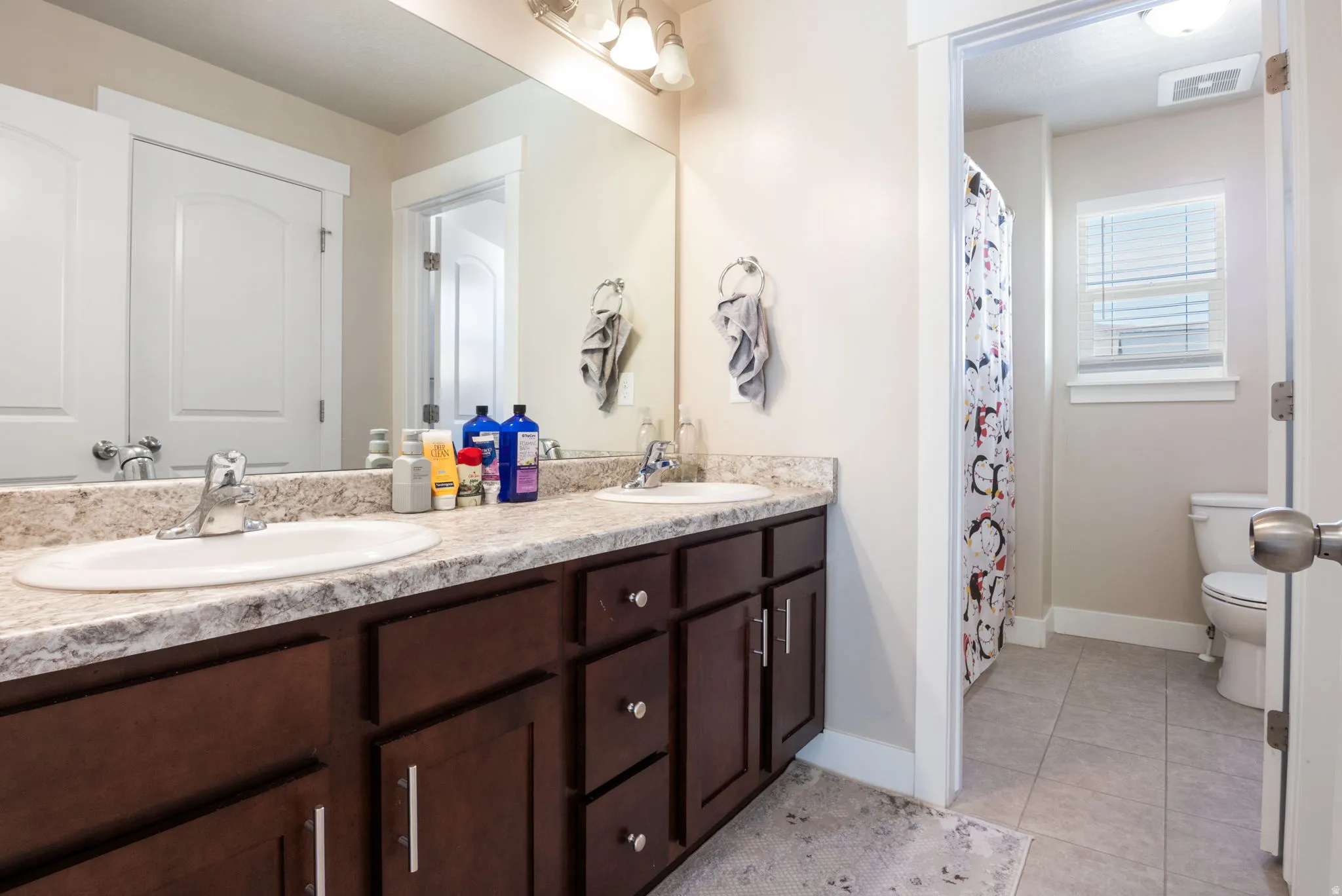 Full bathroom featuring double vanity, curtained shower, and light tile patterned floors