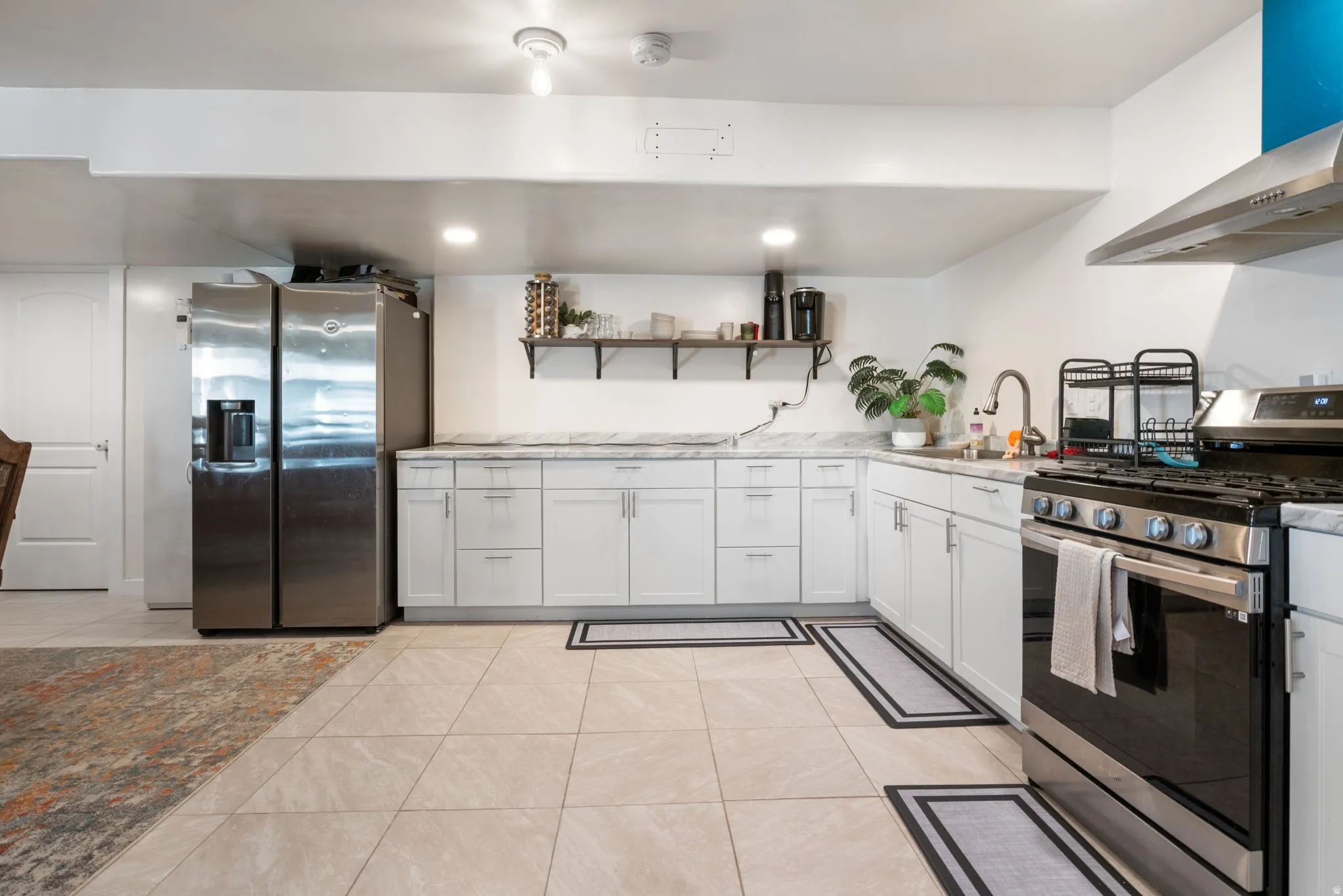 Kitchen featuring stainless steel appliances, open shelves, range hood, light tile patterned floors, and light stone countertops
