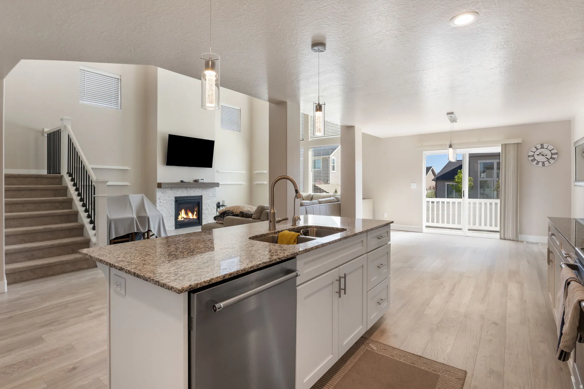 Kitchen featuring open floor plan, a lit fireplace, stainless steel appliances, hanging light fixtures, and light stone countertops