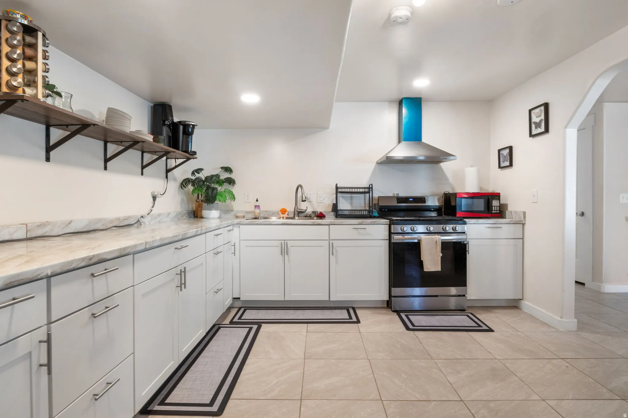 Kitchen with open shelves, gas range, arched walkways, light stone counters, and recessed lighting